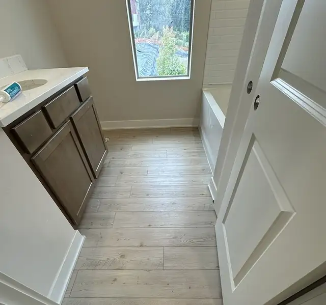 Wood-look plank tile floor in a bathroom with dark wood vanity and white door