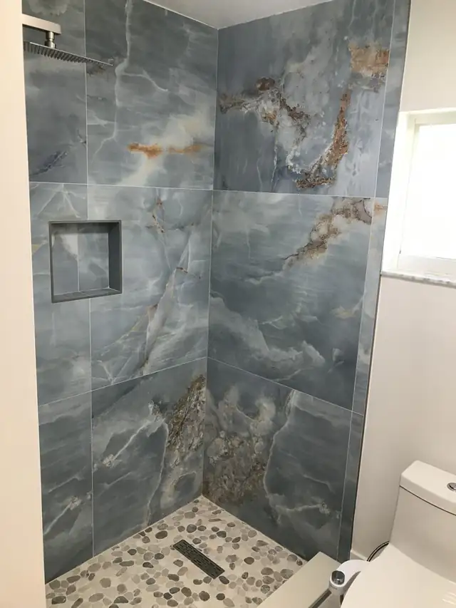 Shower with blue-gray marble-look porcelain tile and recessed niche after a new shower pan
