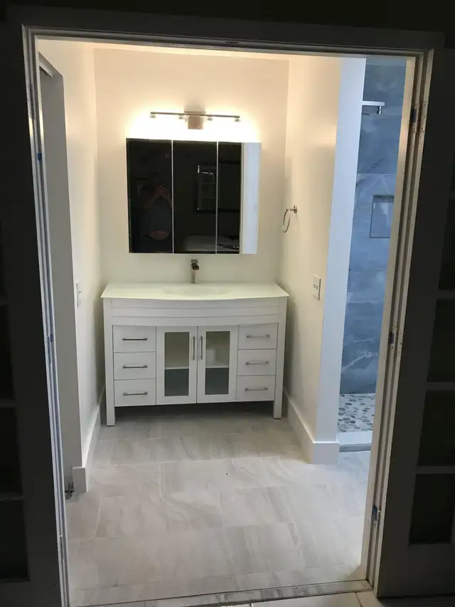 White bathroom vanity with mirror cabinet and blue-gray tiled shower wall beside it