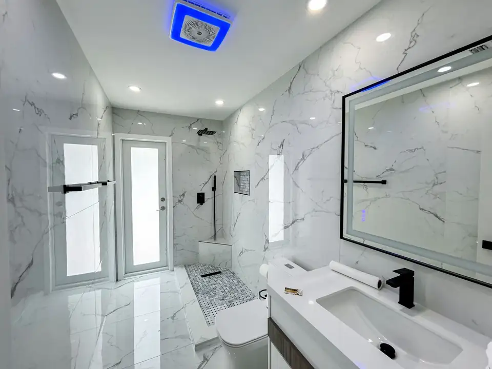 Guest bathroom with white marble-look tile, floating vanity, lit mirror and black fixtures by J&M, which offers bathroom remodeling in Palmetto Bay, FL