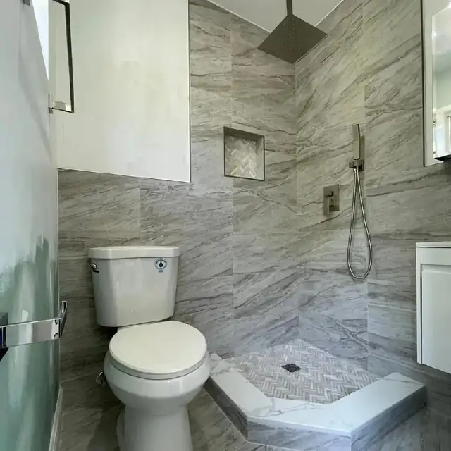Gray marble-look tiled shower with niche, handheld shower and low curb